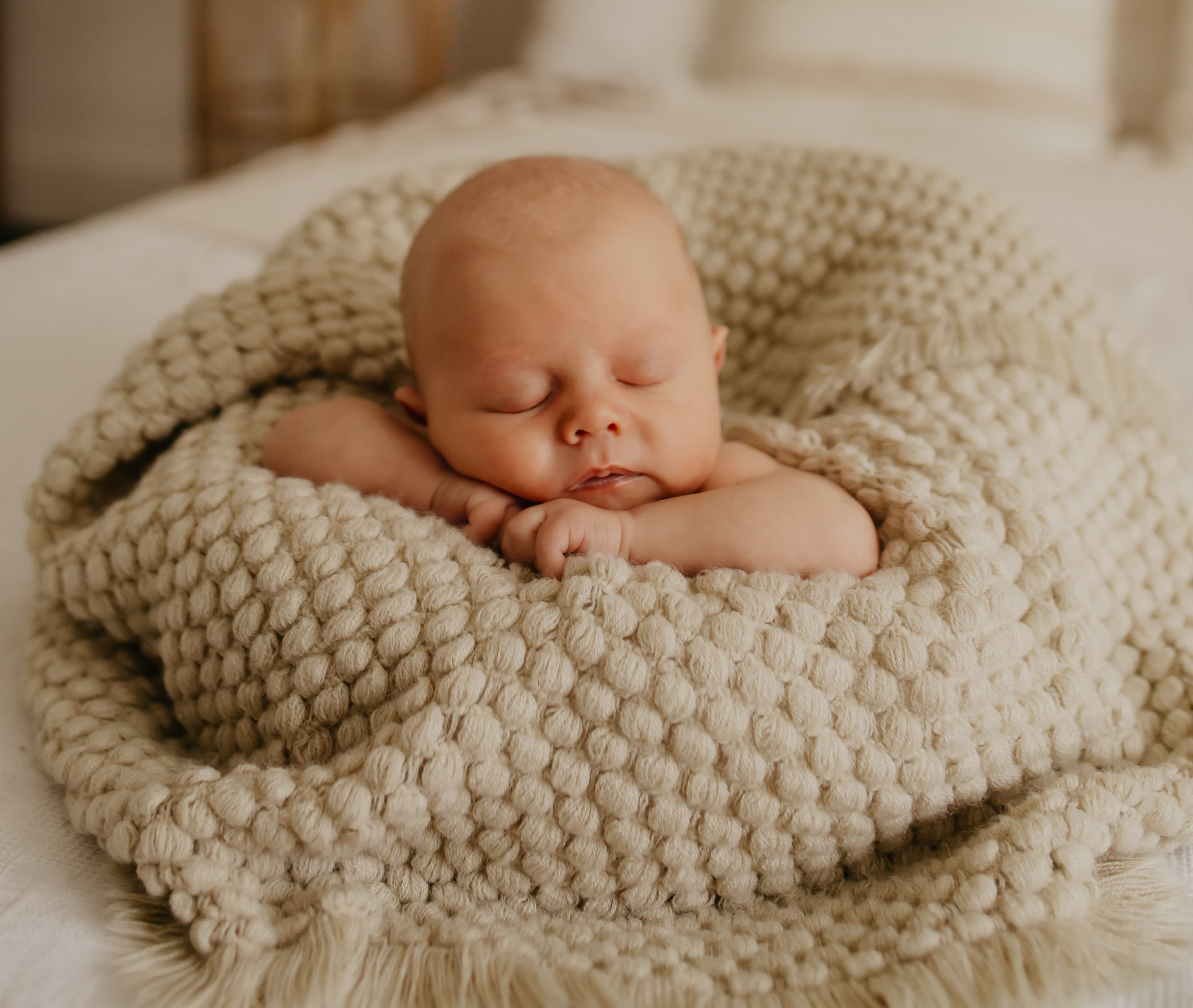 Peaceful newborn baby sleeping in a cozy cream-colored knitted blanket, representing the gentle care provided during newborn visits